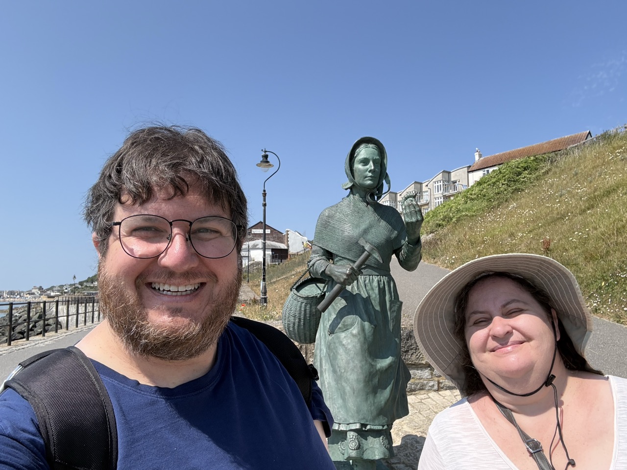 Picture of two people in front of a green bronze statue; the statue shows a woman in a bonnet holding a fossil in her hand and with a basket on her hip